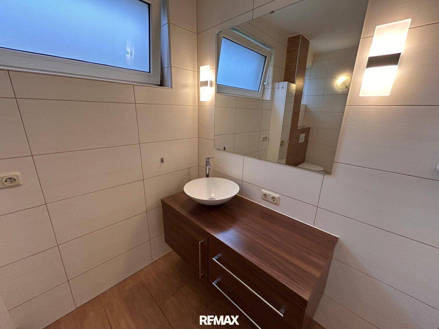 Badezimmer mit modernem Waschtisch, großem Spiegel und zwei Fenstern, hell und funktional.