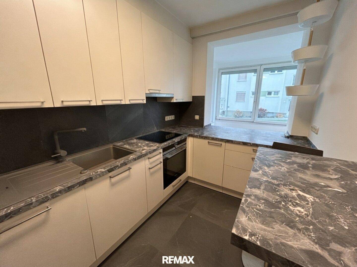 Moderne Einbauküche mit dunklen Arbeitsplatten und hellen Schränken, ausgestattet mit Kochfeld und Ofen.