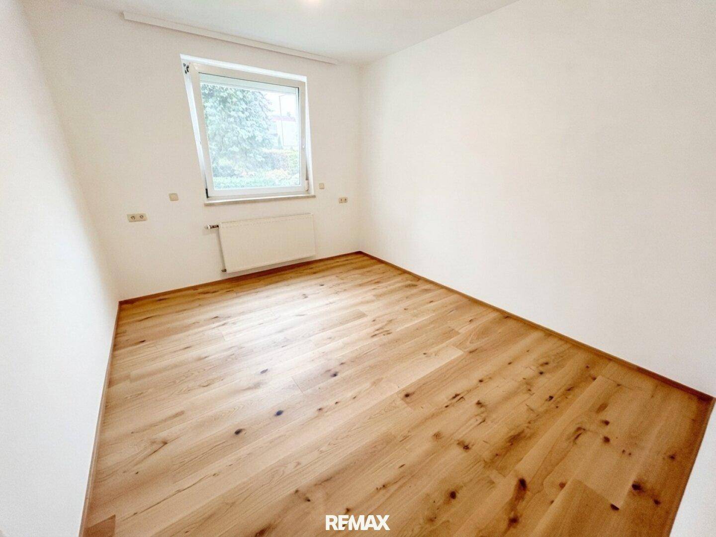 Helles Schlafzimmer mit Parkettboden und einem Fenster mit Blick ins Grüne, unmöbliert und geräumig.