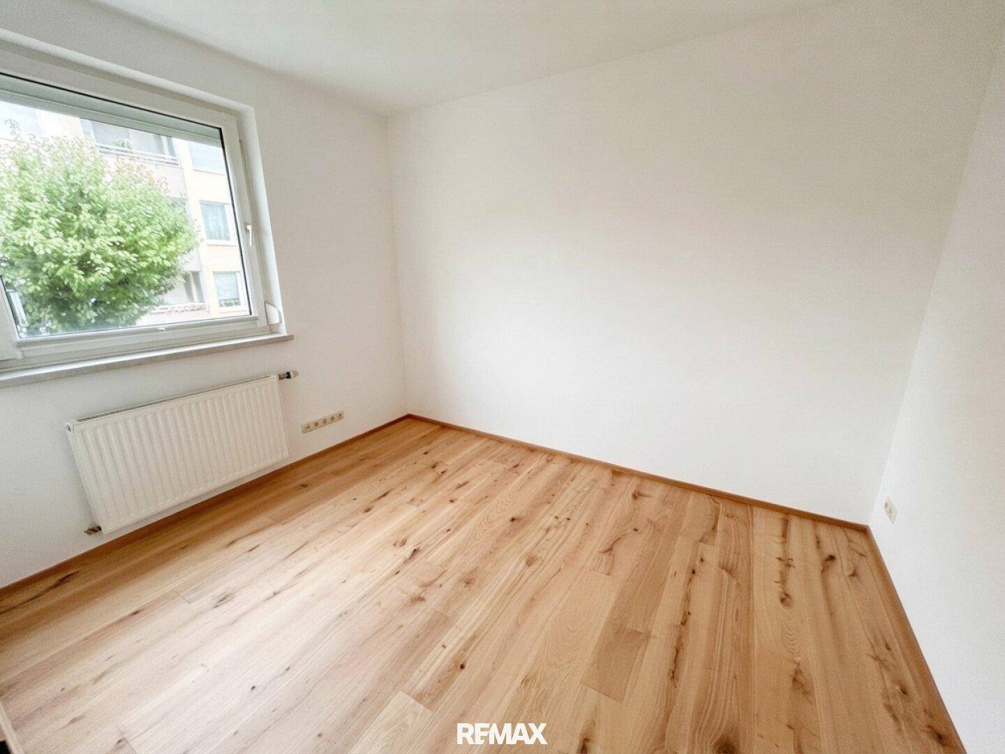 Geräumiges Schlafzimmer mit hellem Parkettboden und großem Fenster, das viel Tageslicht bietet.