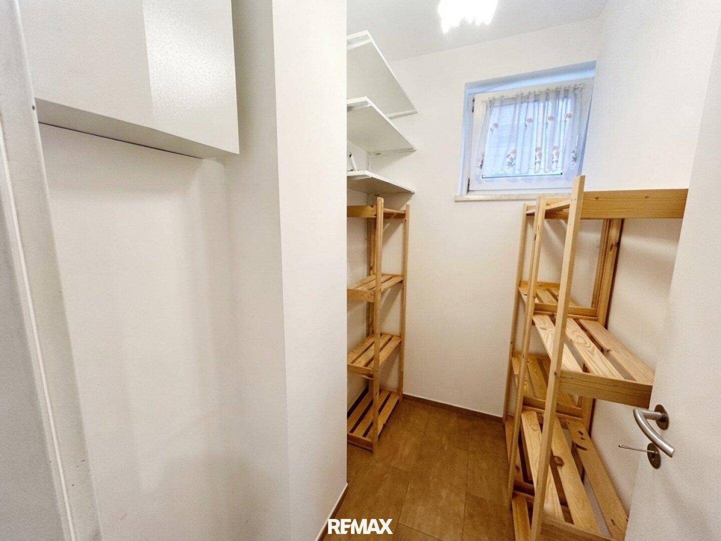 Praktischer Abstellraum mit Holzregalen und einem kleinen Fenster, ideal für Vorräte oder Haushaltsgegenstände.