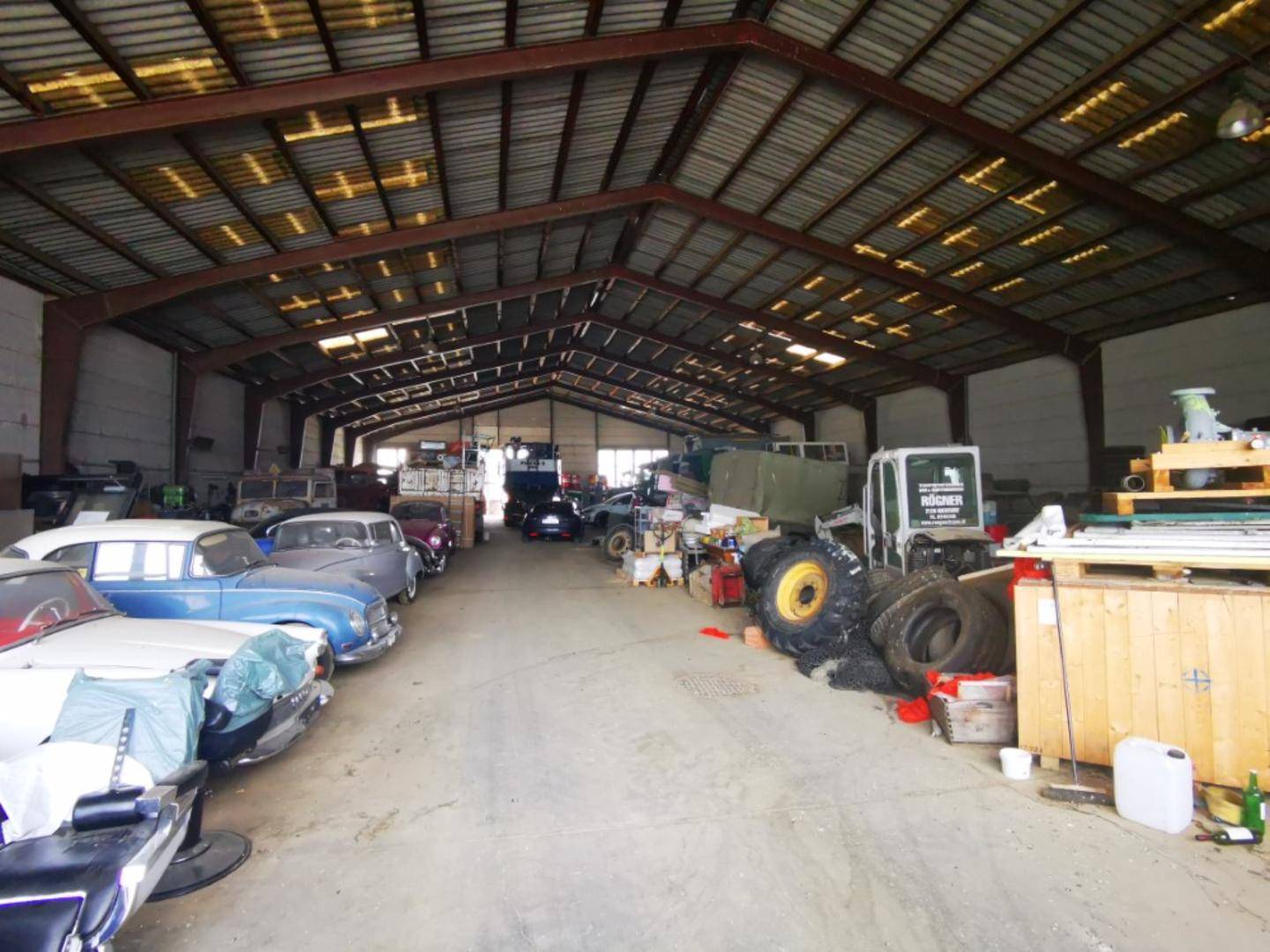 Geräumige Industriehalle mit hoher Decke, genutzt als Lager für diverse Fahrzeuge und Arbeitsgeräte.