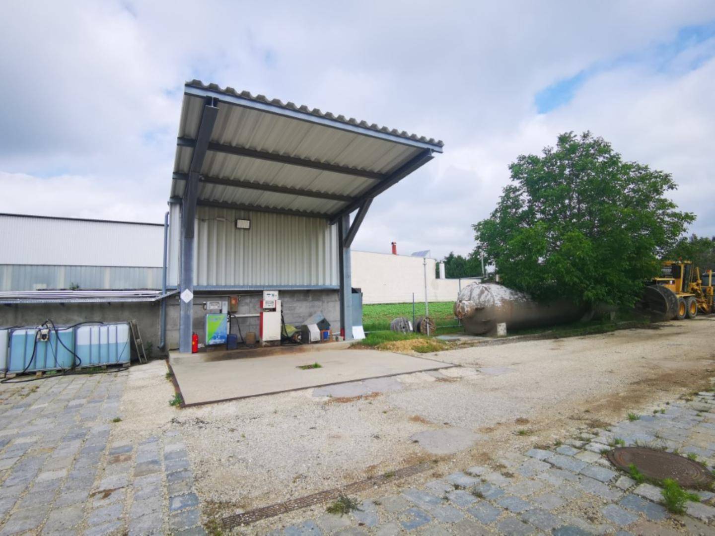 Überdachte Tankstelle auf dem Betriebsgelände mit Zapfsäulen und einem großen Lagertank im Hintergrund.
