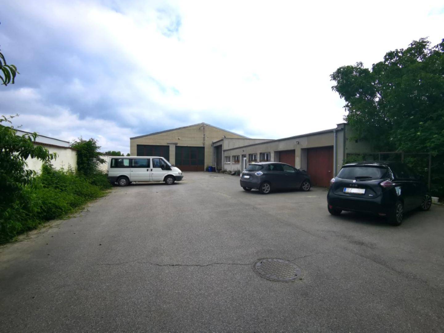 Außenansicht des Betriebsgeländes mit mehreren Hallen und einem großen asphaltierten Vorplatz für Fahrzeuge.