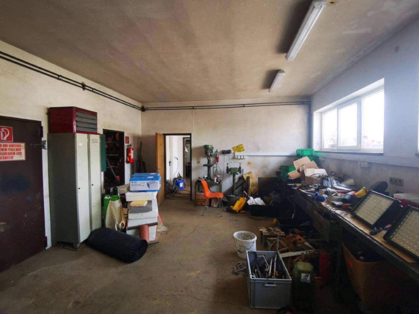 Funktionale Werkstatt mit Arbeitsbänken, Werkzeugen und Fenstern, die für natürliches Licht sorgen.