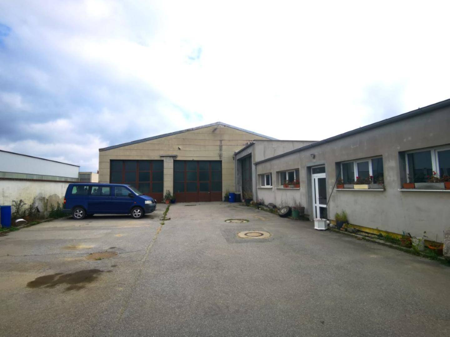 Blick auf die Gebäude des Betriebsgeländes mit breiter Zufahrt und Parkmöglichkeiten vor den Hallen.