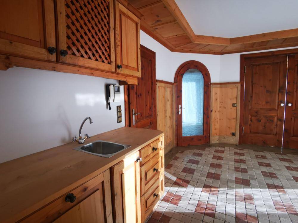 Kleine Küchenzeile mit Spülbecken, Holzschränken und rustikalem Fliesenboden in einem Durchgangsbereich.