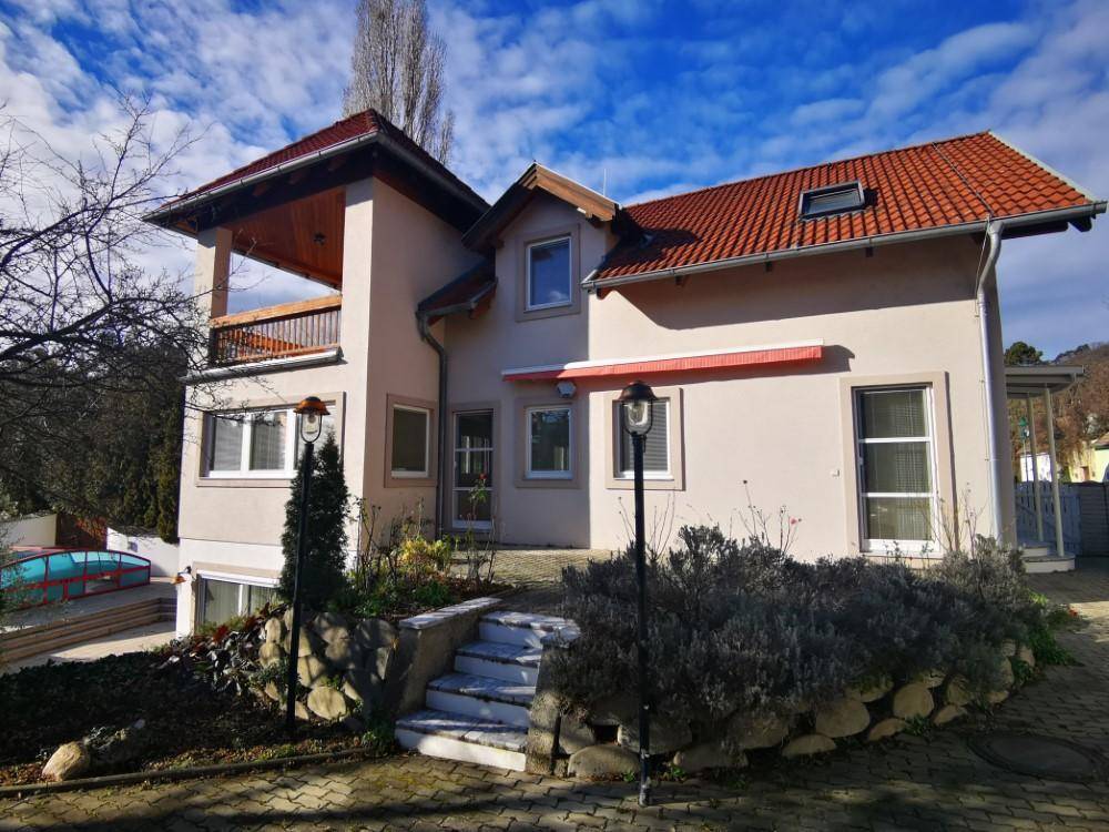 Attraktive Hausfassade mit rotem Ziegeldach, Balkon und gepflegtem Vorgartenbereich.