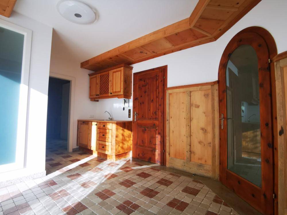 Helle Küchenzeile mit Holzmöbeln und gemustertem Fliesenboden, durchflutet von Sonnenlicht.