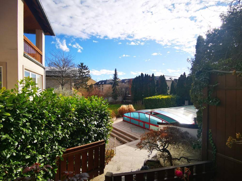 Weitläufiger Gartenbereich mit überdachtem Pool und viel Grün unter strahlend blauem Himmel.