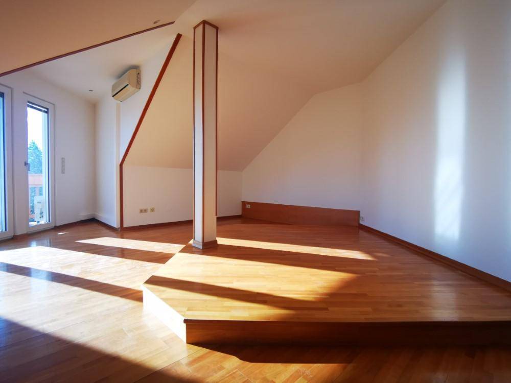 Lichtdurchflutetes Dachzimmer mit Holzboden und erhöhter Plattform, ideal als Schlaf- oder Arbeitsbereich.