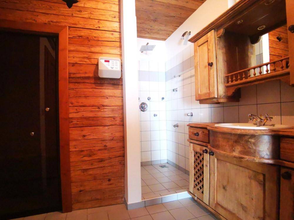 Rustikales Badezimmer mit Holztäfelung, Duschbereich und Waschtisch mit Holzunterschrank und Fliesen.