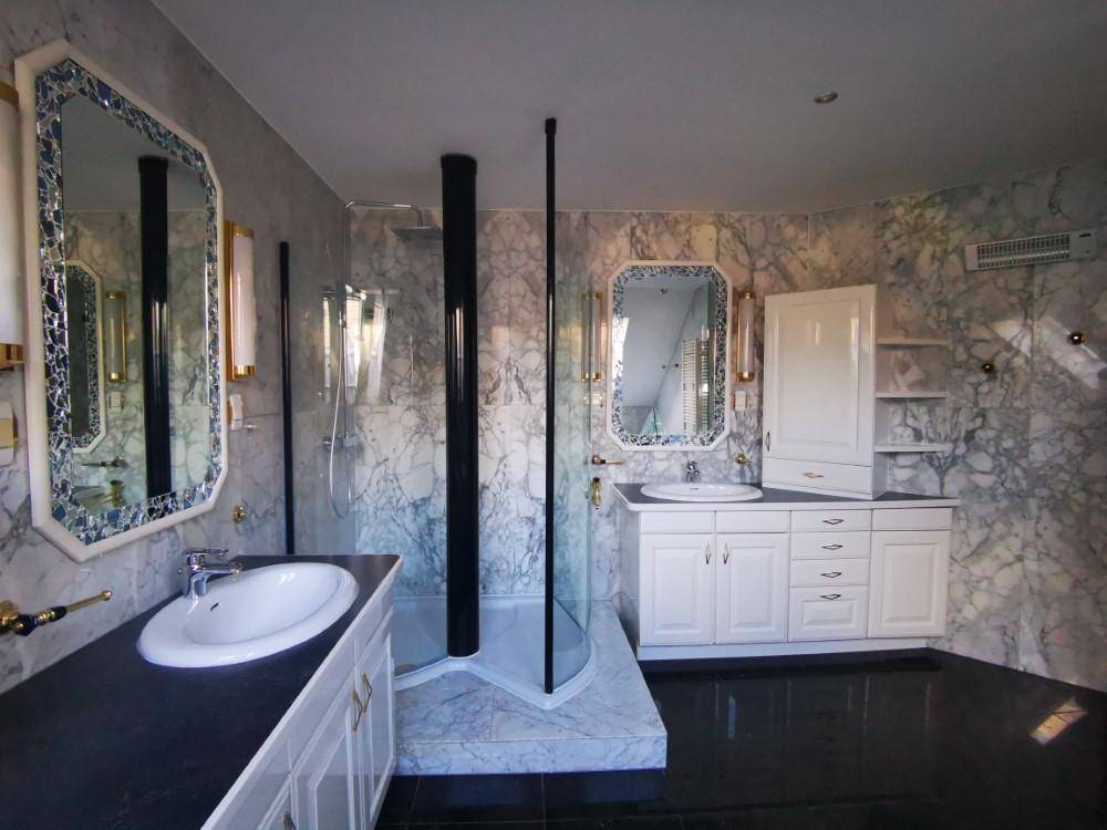 Elegantes Badezimmer mit Marmorwänden, Doppelwaschbecken und moderner Duschkabine.