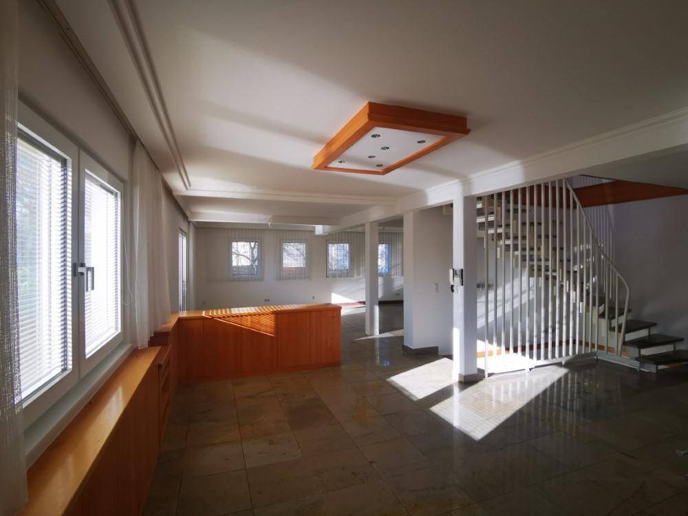 Geräumiger Wohnbereich mit Treppe und dekorativer Deckenbeleuchtung, durchflutet von Sonnenlicht.