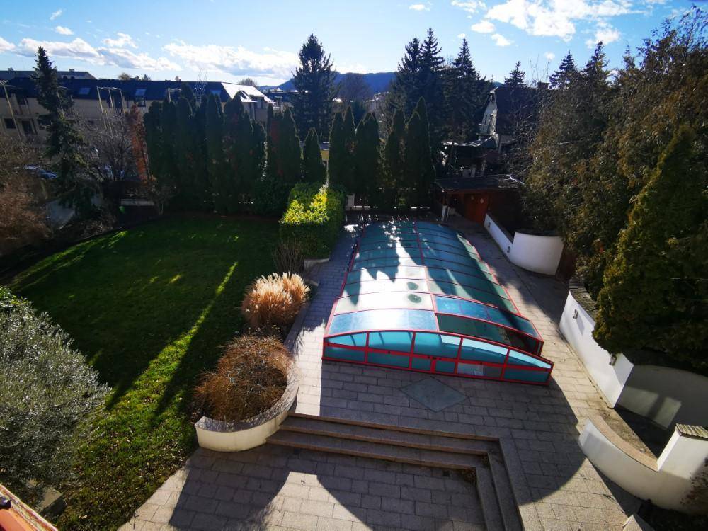 Panoramablick auf den weitläufigen Garten mit Rasenfläche und dem überdachten Poolbereich.