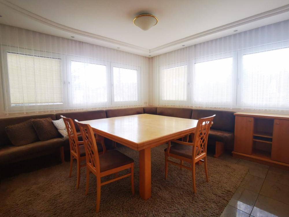 Gemütlicher Essbereich mit großem Holztisch und Eckbank, umgeben von Fenstern.