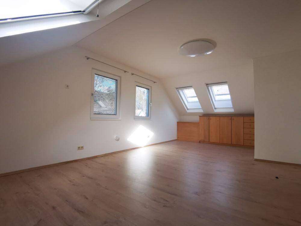 Helles Dachzimmer mit Laminatboden, Dachfenstern und eingebauten Holzschränken.
