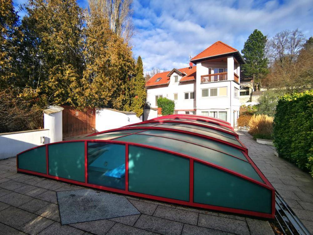 Überdachter Swimmingpool im Gartenbereich mit angrenzender Terrasse und Blick auf das Haus.