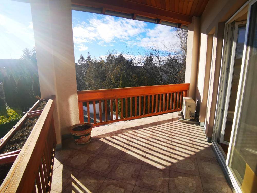 Geräumiger Balkon mit Holzbalken und Fliesenboden, bietet einen schönen Ausblick ins Grüne.