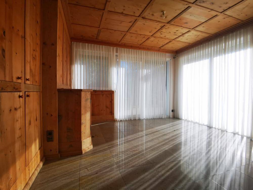 Helles Zimmer mit Holztäfelung, Kassettendecke und großen Fenstern, durch die Sonnenlicht fällt.