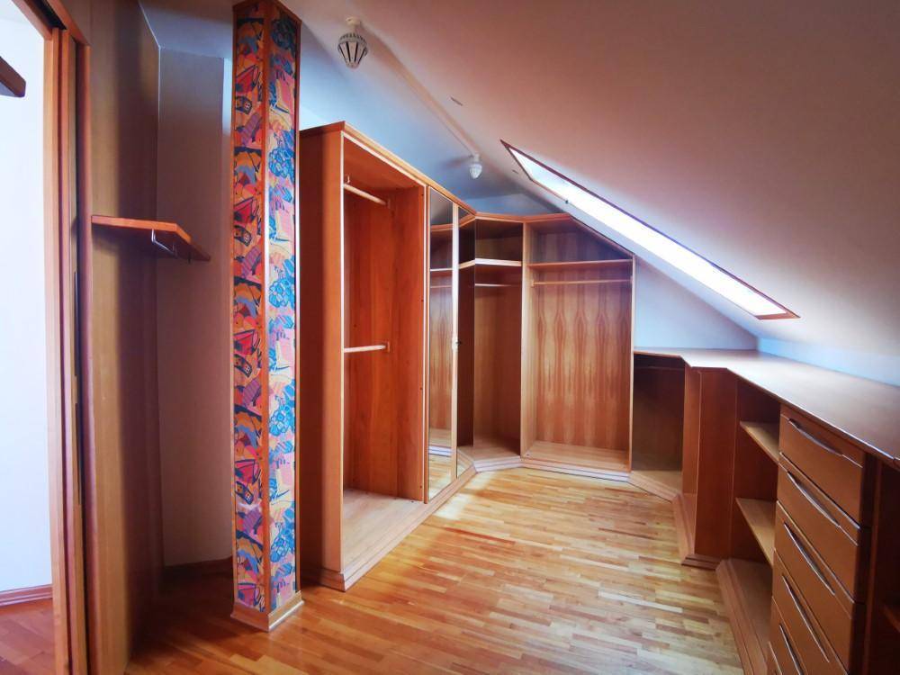 Begehbarer Kleiderschrank im Dachgeschoss mit maßgefertigten Holzschränken und Dachfenster.