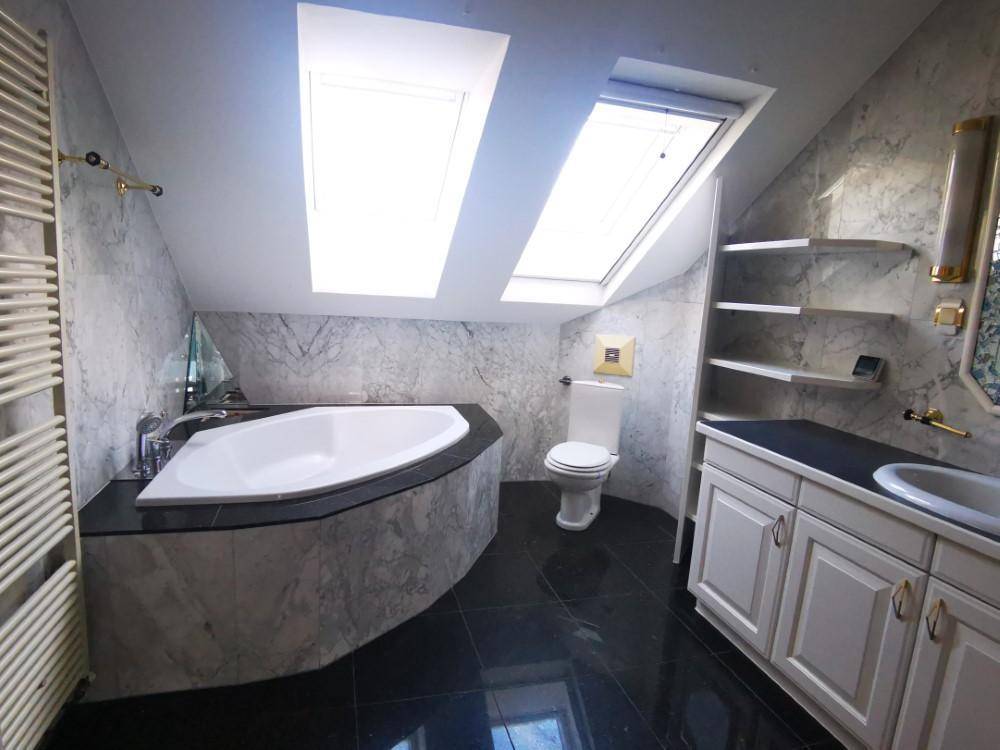 Marmoriertes Badezimmer im Dachgeschoss mit Badewanne, WC und Dachfenstern für natürliches Licht.