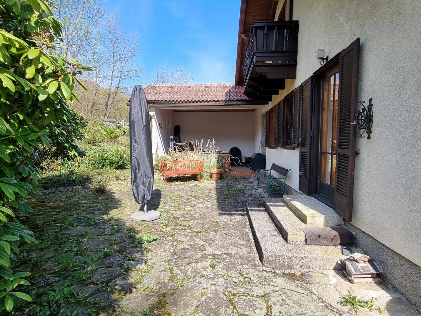 Außenbereich des Hauses mit gepflasterter Terrasse, Garten und Zugang zu einem überdachten Bereich.