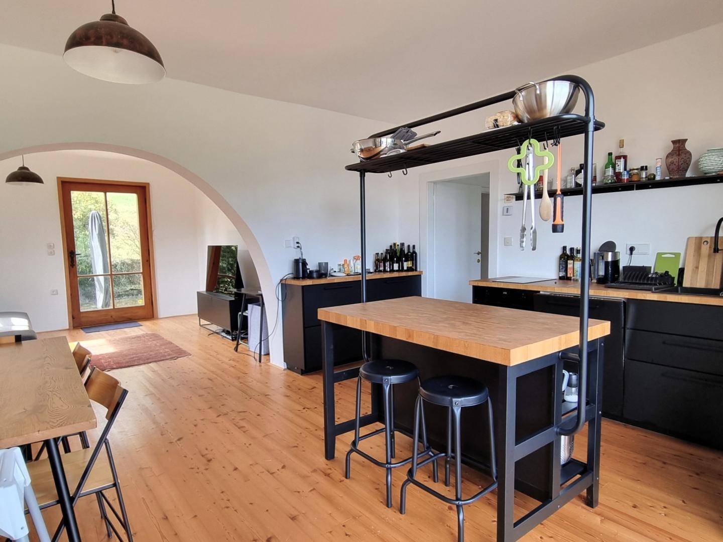 Offene Küche mit schwarzer Einrichtung, Holztheke und Essbereich, verbunden mit dem Wohnzimmer.