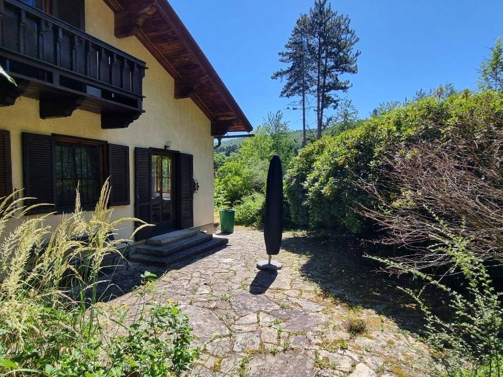 Gepflasterte Terrasse am Haus mit Sonnenschirm und Blick ins Grüne.