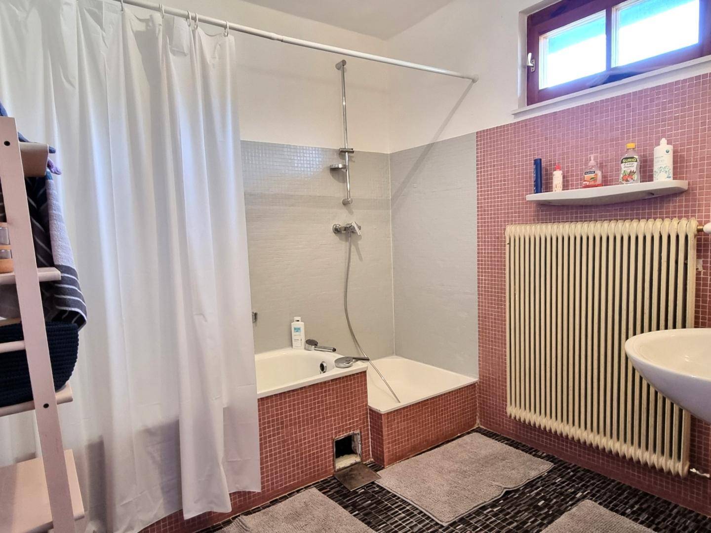 Badezimmer mit Badewanne, Duschvorhang und rosa Mosaikfliesen an den Wänden.