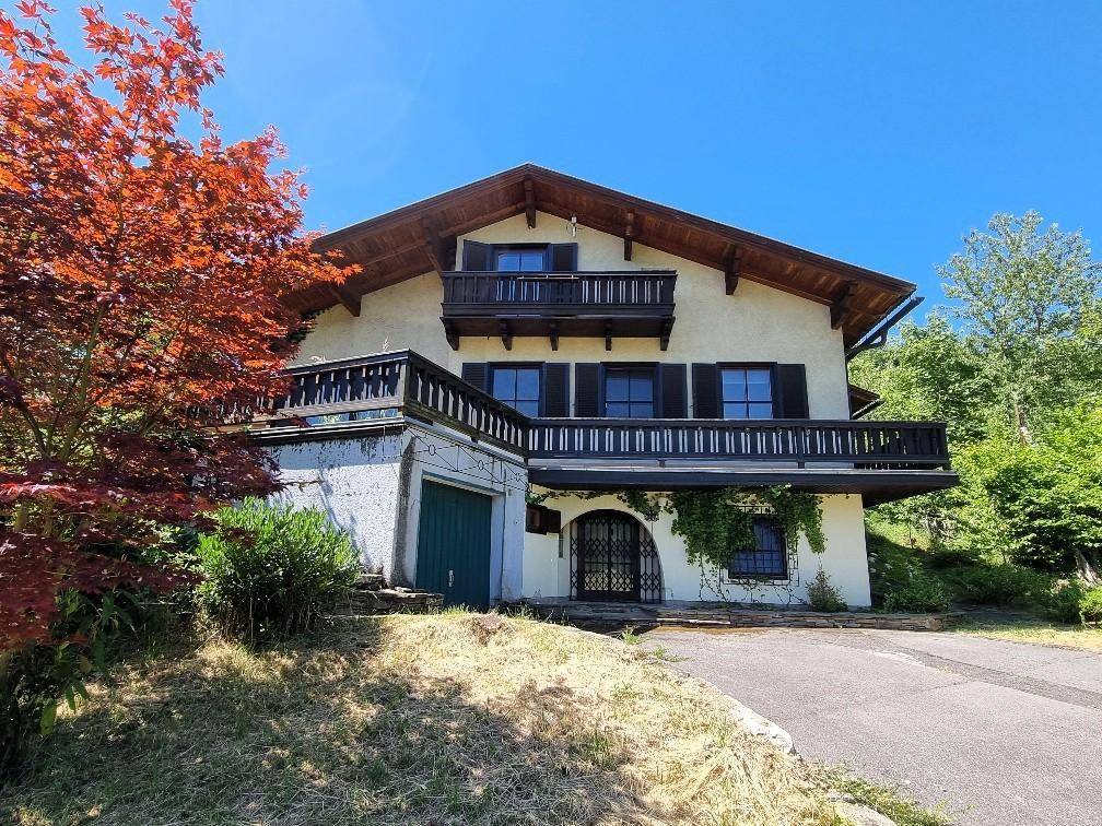 Traditionelles Haus mit Holzbalkonen und dunklen Fensterläden, umgeben von viel Grün.