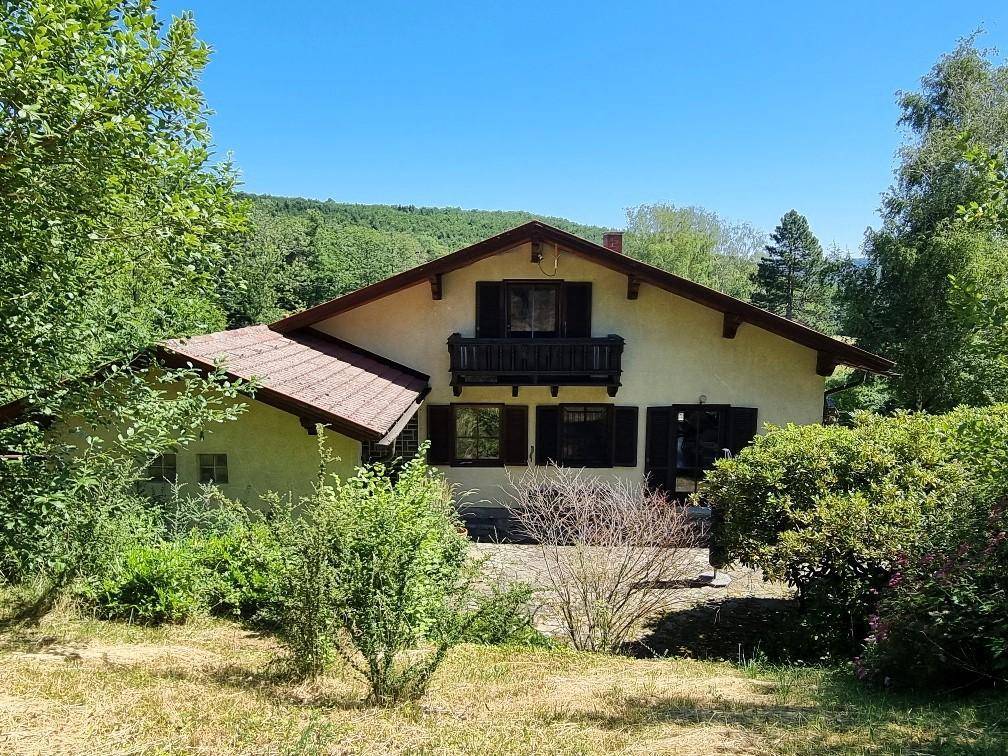Charmantes Landhaus mit Satteldach und Holzbalkonen, umgeben von üppiger Vegetation.