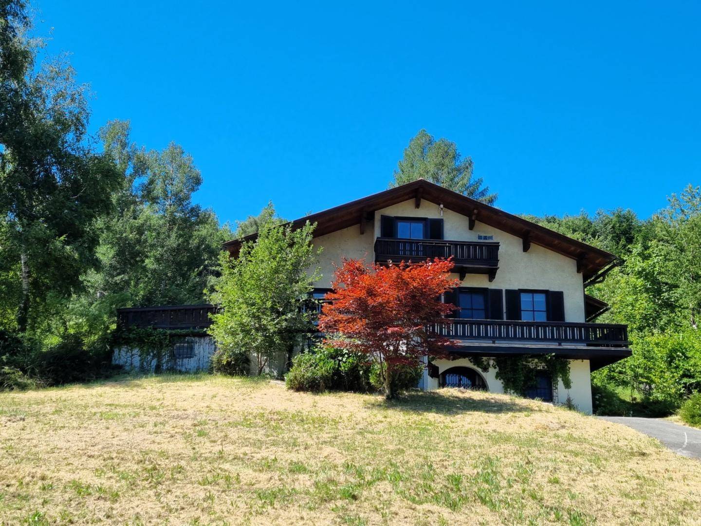 Traditionelles Landhaus mit Holzbalkonen und Fensterläden, eingebettet in eine grüne Umgebung.