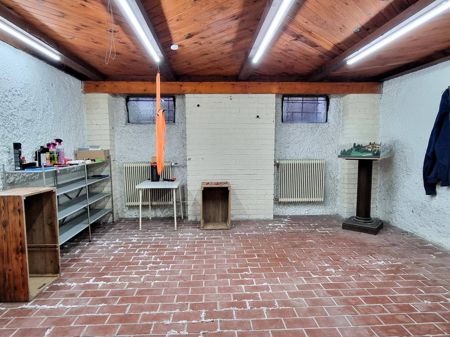 Kellerraum mit Ziegelboden, unverputzten Wänden und sichtbaren Holzdeckenbalken.