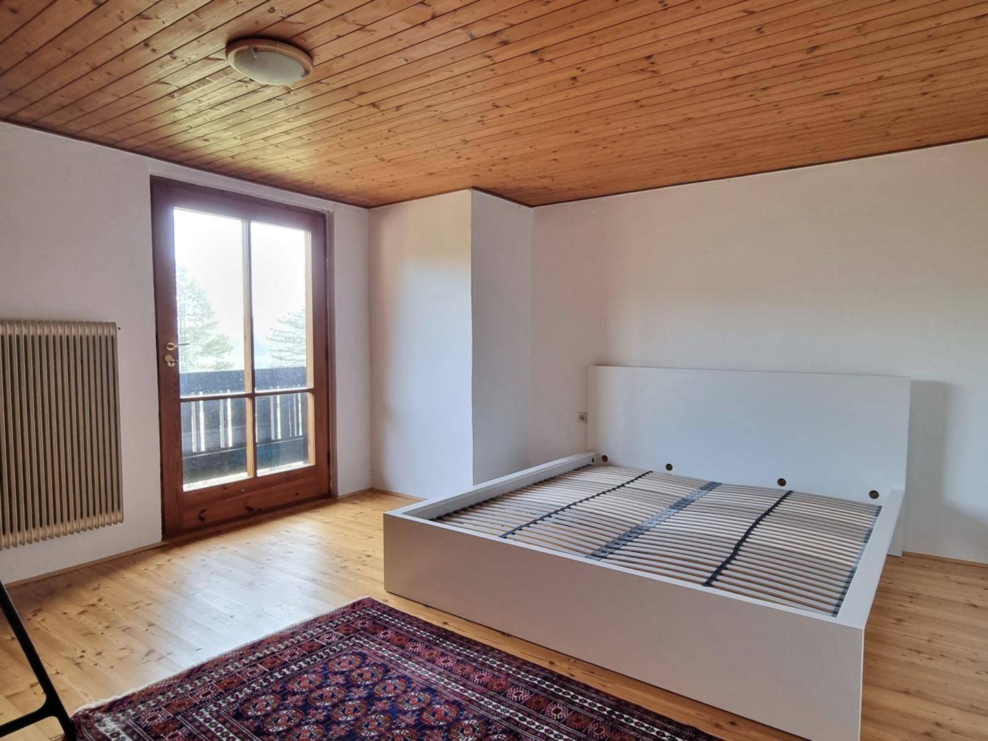 Schlafzimmer mit Holzboden, Holzdecke und einem großen Fenster mit Balkonzugang.