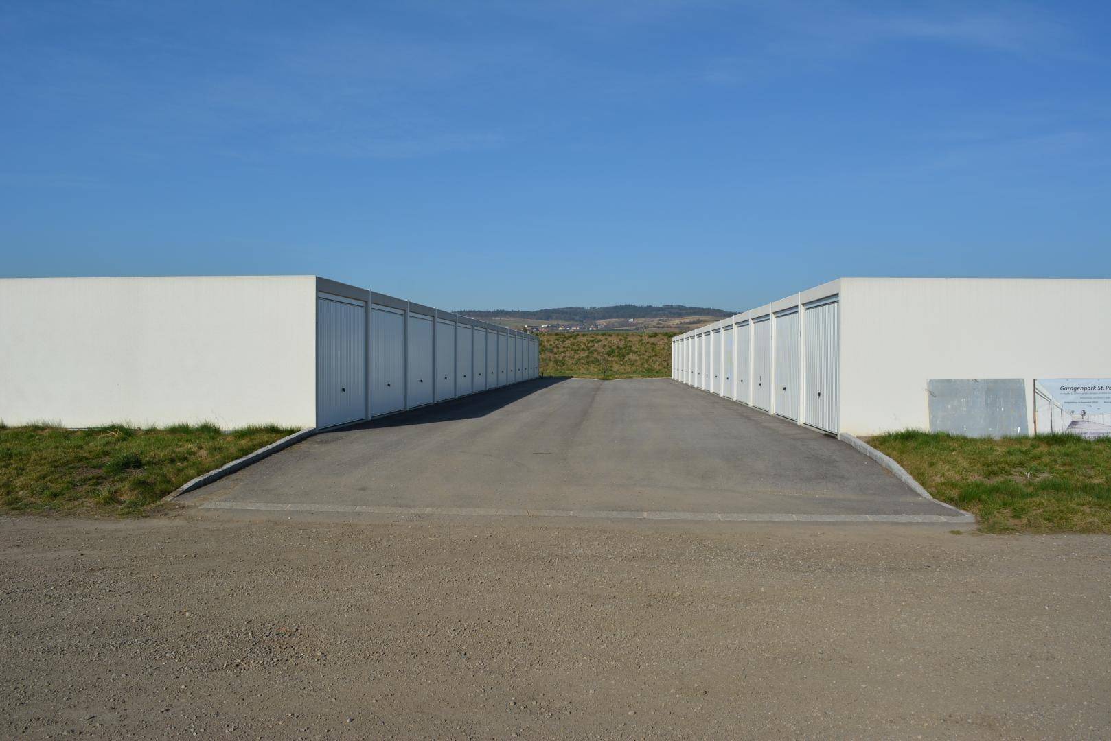 Reihen von modernen Lagerhallen oder Garagen mit Zufahrtsweg unter blauem Himmel.
