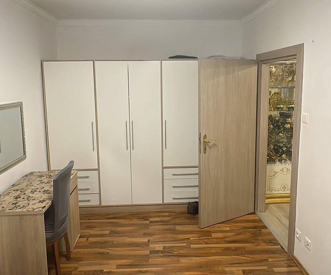 Schlafzimmer mit großem Einbauschrank, Schreibtisch und dunklem Laminatboden.