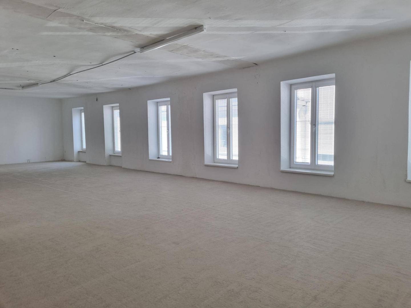 Geräumiger, leerer Raum mit vielen Fenstern und einem rohen Boden, ideal für individuelle Gestaltung.