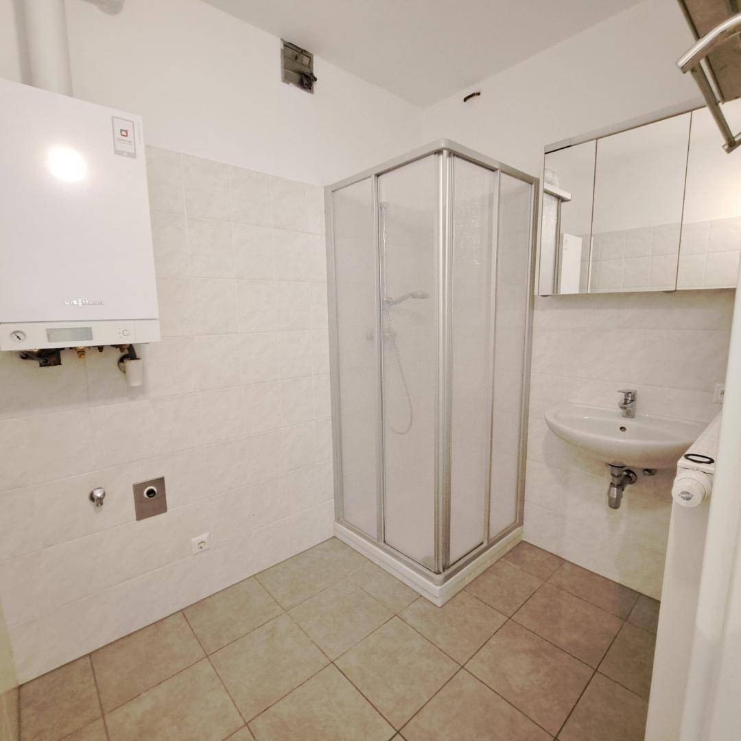 Badezimmer mit Duschkabine, Waschbecken, Spiegelschrank und Warmwasserbereiter.