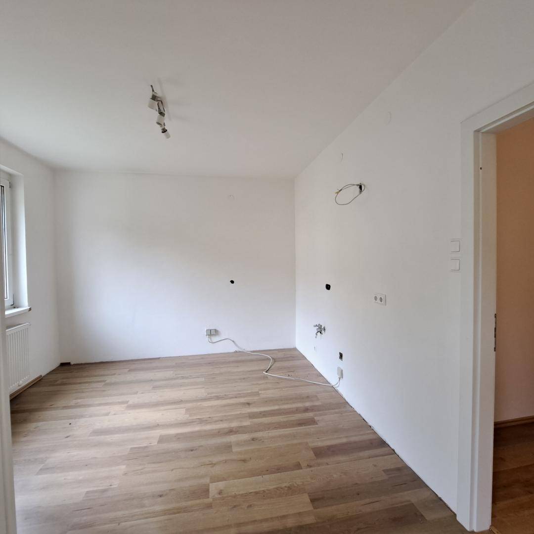 Leerer Küchenbereich mit vorbereiteten Anschlüssen für Geräte und hellem Parkettboden.