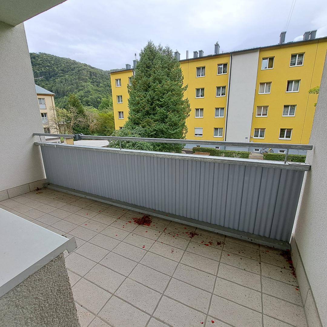 Balkon mit Fliesenboden und Blick auf den grünen Innenhof und die umliegenden Gebäude.