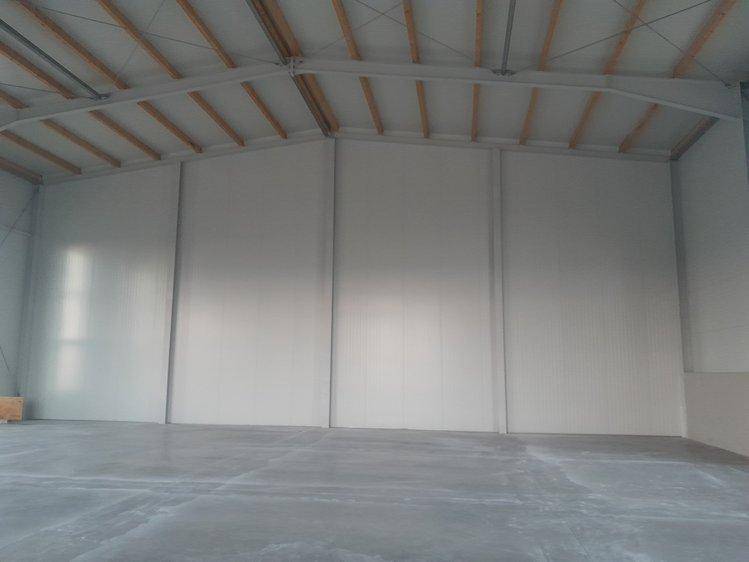 Geräumiger, leerer Industrieraum mit Betonboden, hellen Wänden und sichtbarer Dachkonstruktion.