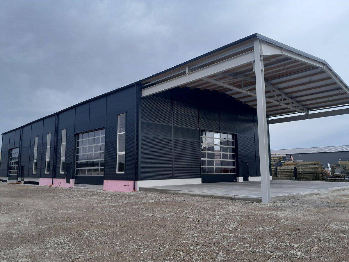 Gesamtansicht des neuen Industriegebäudes mit mehreren Glasrolltoren und einem großen überdachten Bereich.