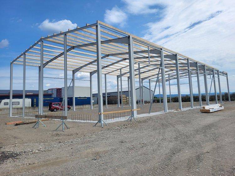Stahlrahmenkonstruktion eines im Bau befindlichen Gebäudes mit sichtbaren Holzdachlatten unter blauem Himmel.