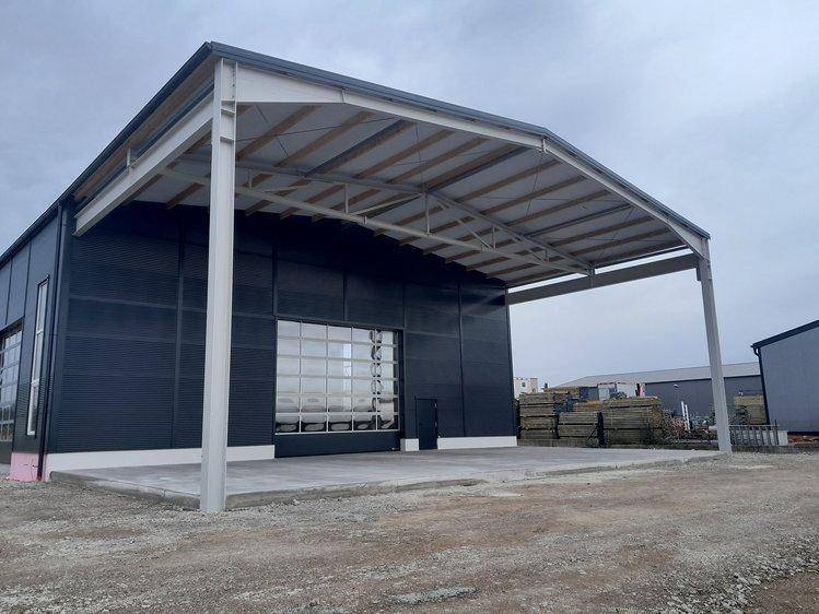 Ansicht des neuen Industriegebäudes mit großem Vordach, dunkelgrauer Fassade und Glasrolltor.