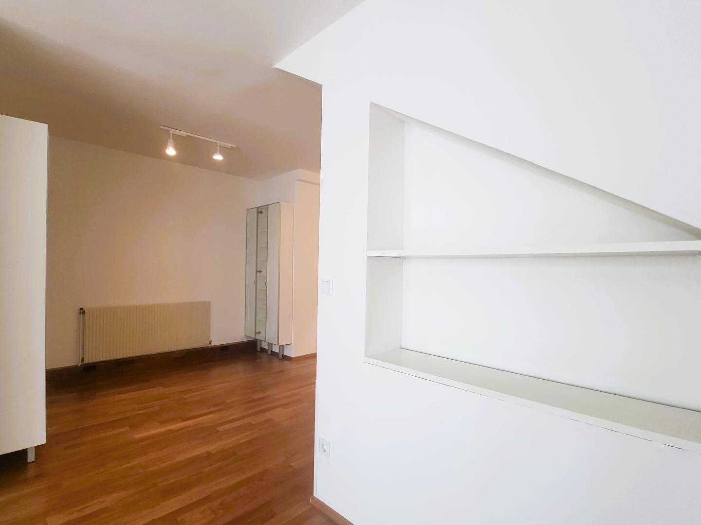 Leeres Wohnzimmer mit Holzboden, Heizkörper und großem Fenster für viel natürliches Licht.