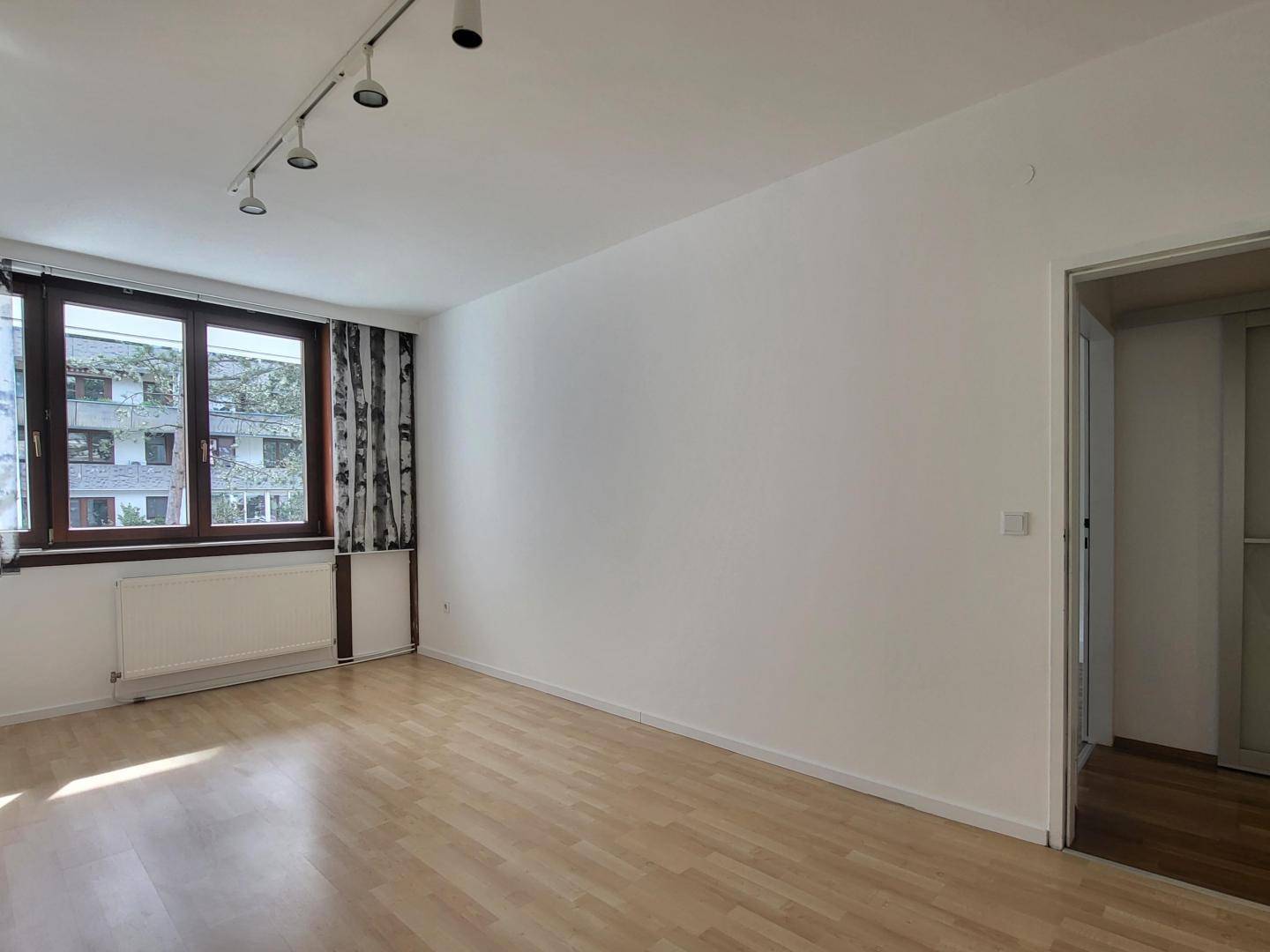 Helles Zimmer mit Laminatboden, großem Fenster und Heizkörper, vielseitig nutzbar.