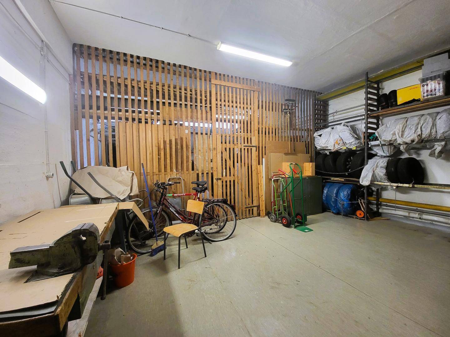 Geräumiger Abstellraum oder Werkstatt mit Holzabtrennung, Regalen und Lagerfläche.