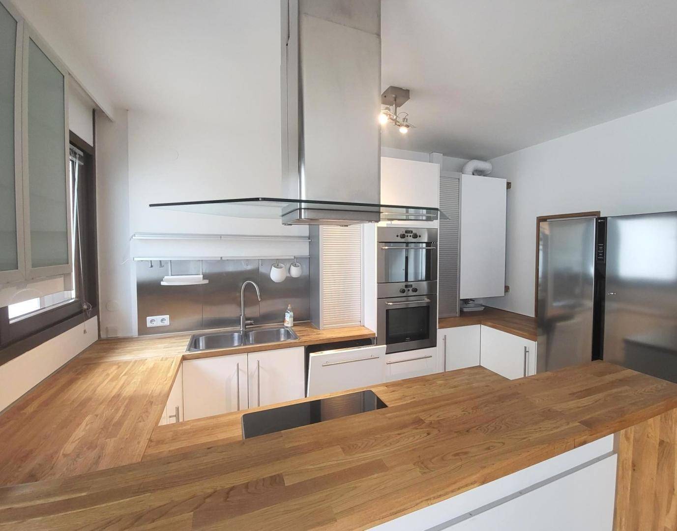 Moderne Einbauküche mit Holz-Arbeitsplatten, Edelstahlgeräten und Spülbecken unter dem Fenster.