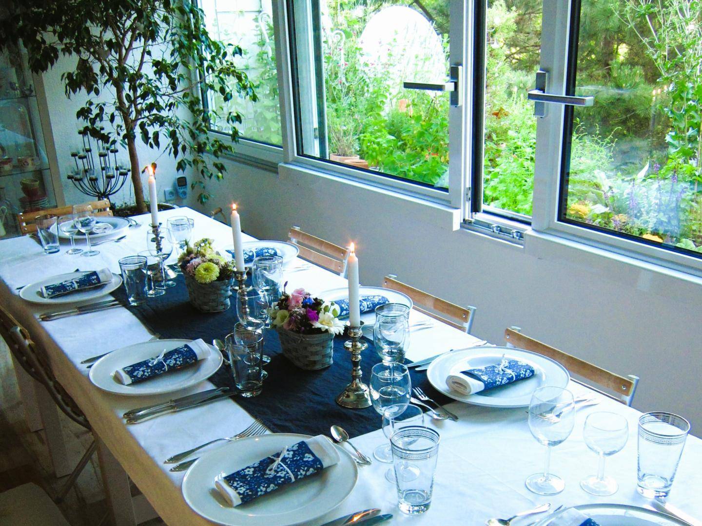 Festlich gedeckter Esstisch in einem hellen Wintergarten mit Blick ins Grüne.